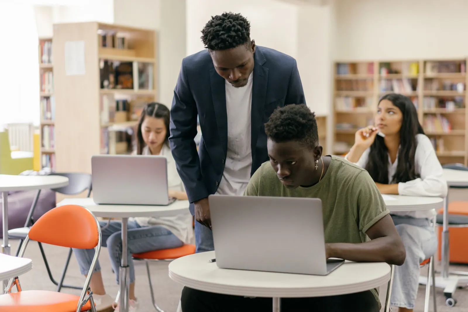 Students working on laptops with a mentor in a bright classroom